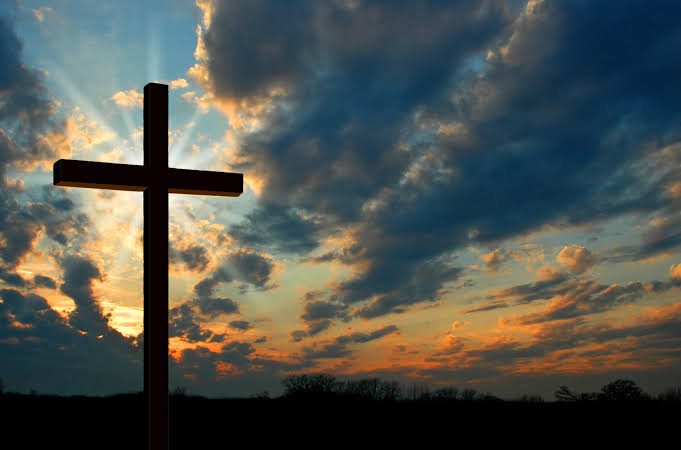A cross silhouetted against a bright evening sky